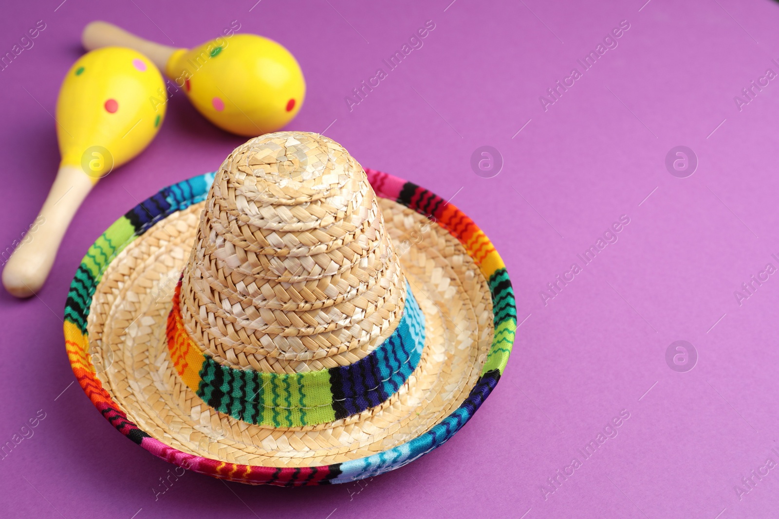 Photo of Mexican sombrero hat and maracas on purple background. Space for text