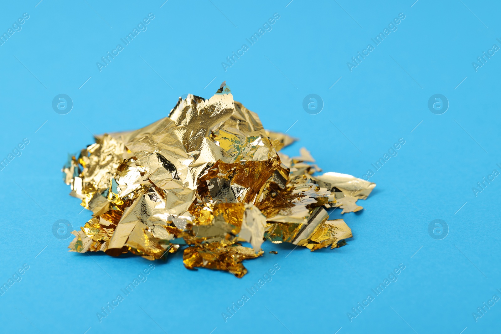 Photo of Pieces of edible gold leaf on light blue background, closeup