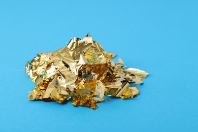 Photo of Piecesedible gold leaf on light blue background, closeup