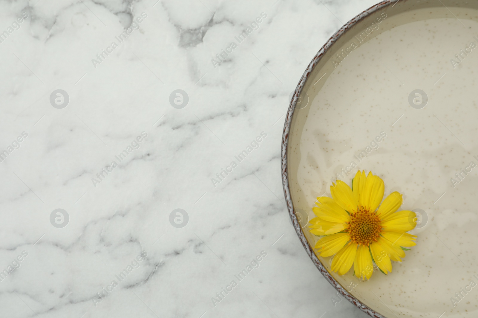 Photo of Beige bowl with water and yellow flower on white marble table, top view. Space for text