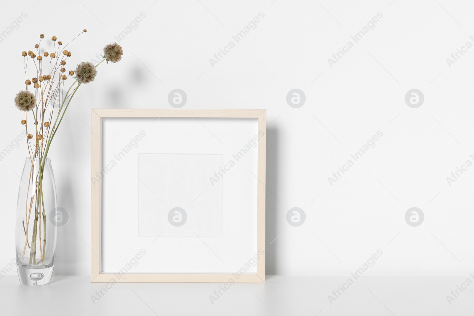 Photo of Empty photo frame and vase with dry decorative flowers on white table. Mockup for design