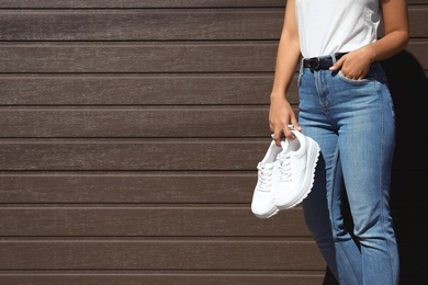 Woman holding stylish sneakers near wooden wall. Space for design