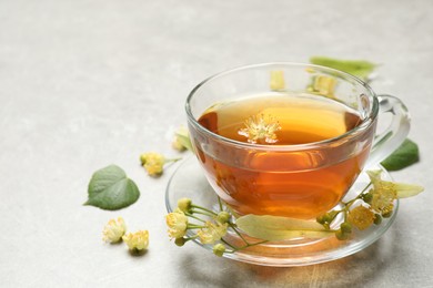 Photo of Cup of tea and linden blossom on light grey table. Space for text