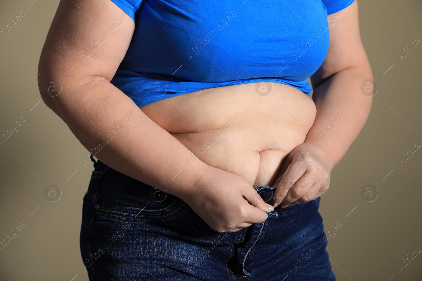 Photo of Overweight woman trying to button up tight jeans on light brown background, closeup