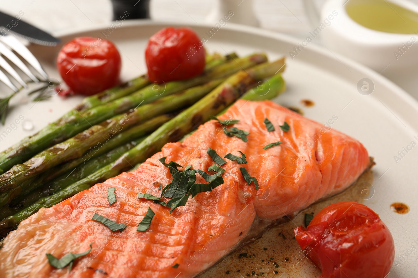 Photo of Tasty grilled salmon with tomatoes, asparagus and spices on table, closeup