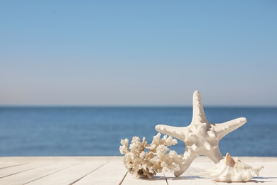 Beautiful starfish, coral and shell on wooden pier near sea. Space for text