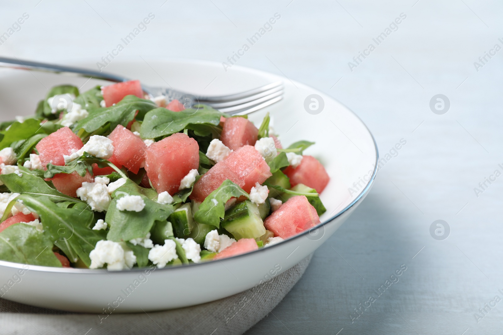 Photo of Delicious salad with watermelon, cucumber, arugula and feta cheese on white table, closeup. Space for text