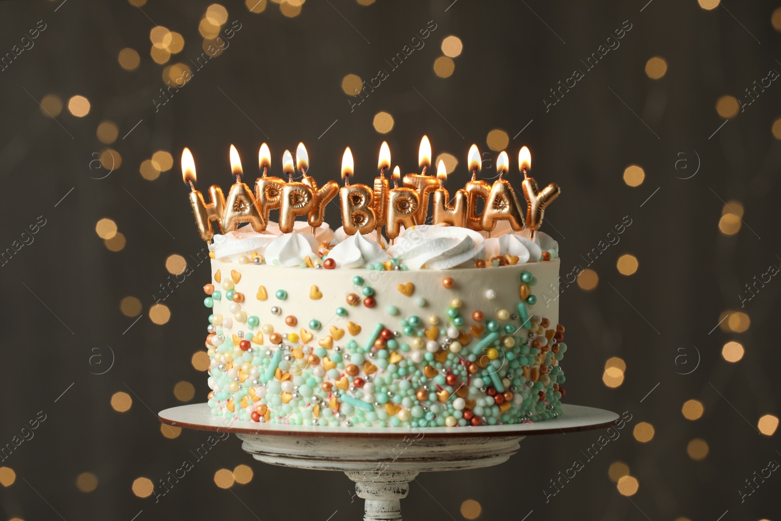 Photo of Beautiful birthday cake with burning candles on stand against festive lights