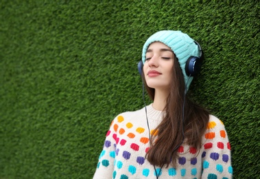 Photo of Beautiful young woman listening to music with headphones near grass wall. Space for text