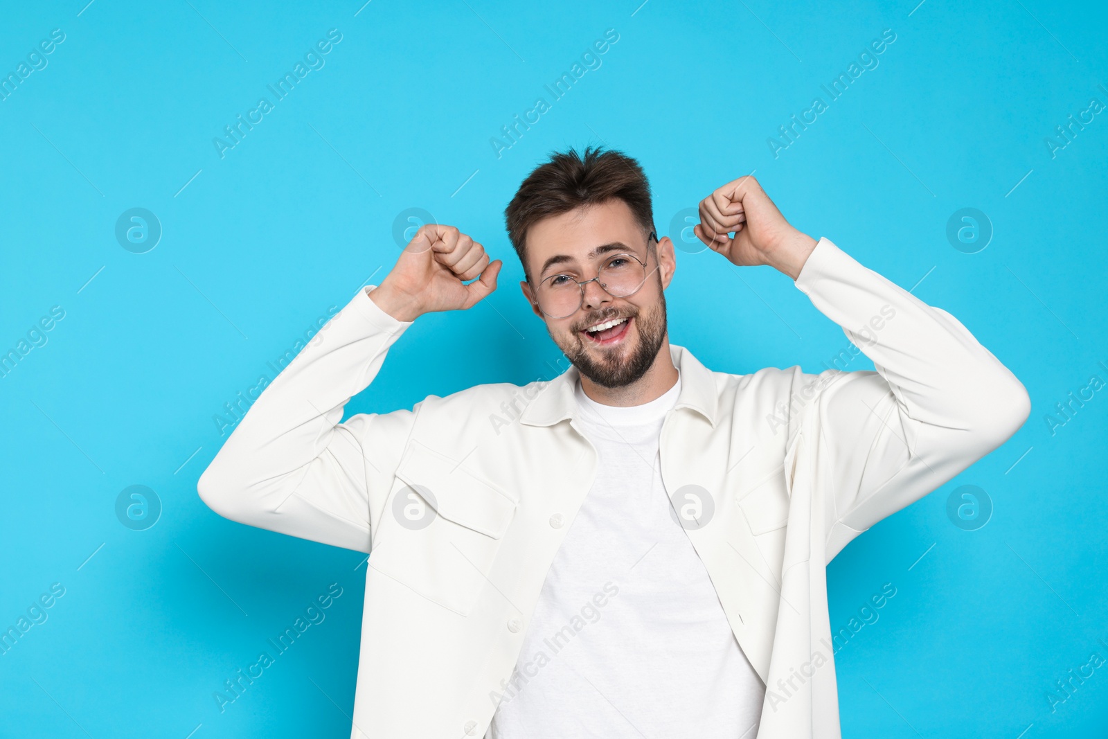 Photo of Excited man in white jacket celebrating victory on light blue background