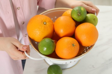 Photo of Woman holding colander with fresh fruits at white marble table, closeup