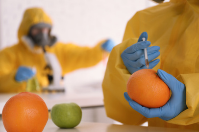 Scientist in chemical protective suit injecting orange at laboratory, closeup