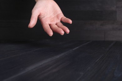 Photo of Woman holding hand above black wooden table, closeup. Space for text