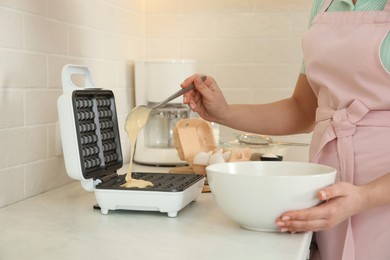 Woman pouring dough onto Belgian waffle maker in kitchen, closeup