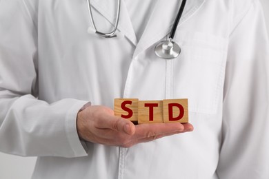 Photo of Doctor holding wooden cubes with abbreviation STD on white background, closeup