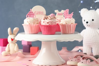 Beautifully decorated baby shower cupcakes for girl with cream and toppers on pink wooden table