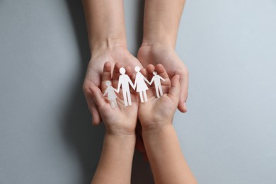 Parents and child holding paper family figures on gray background, top view