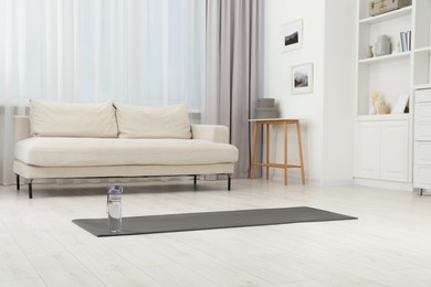 Photo of Yoga mat and bottle of water on floor in room