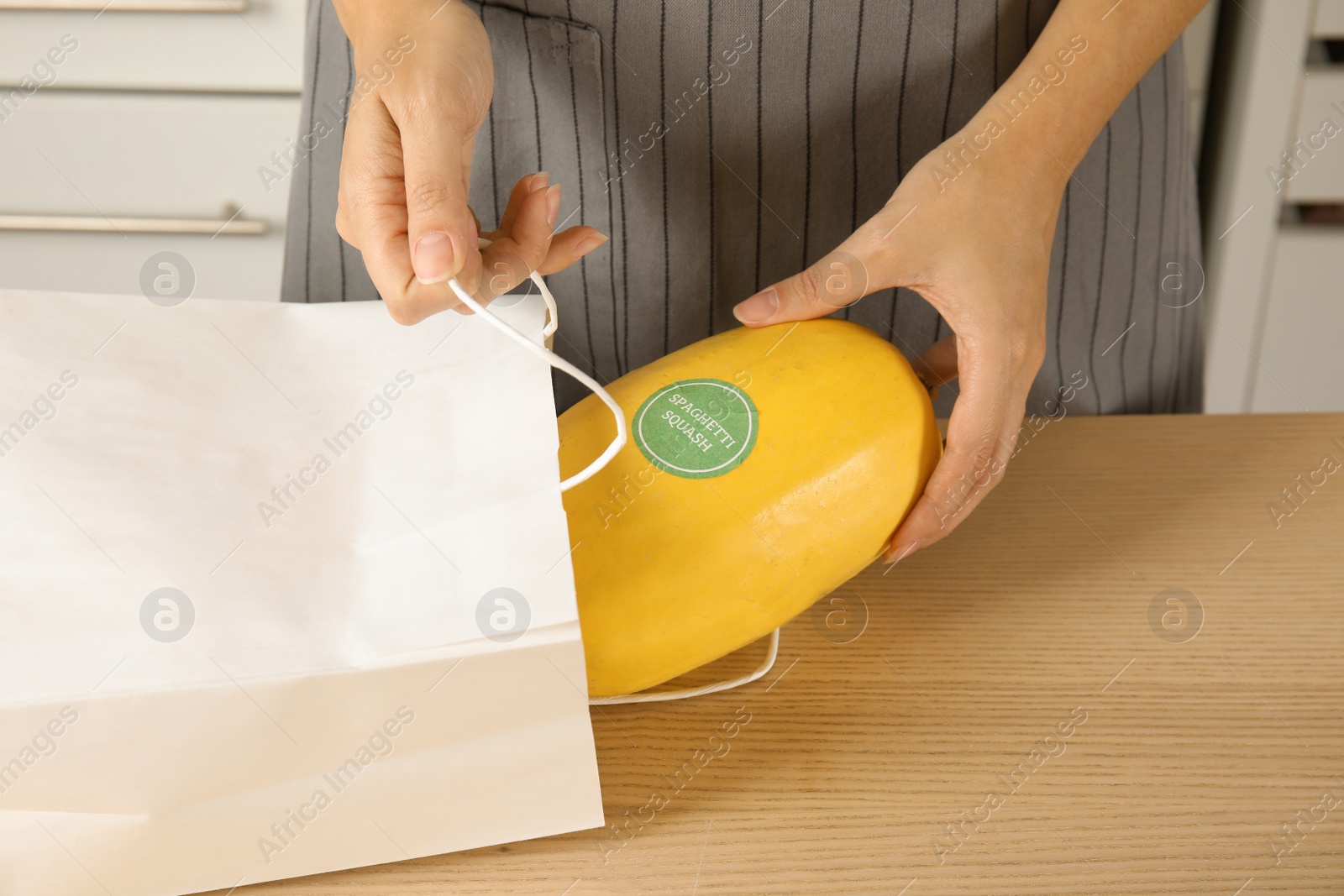Photo of Woman taking spaghetti squash out of shopping bag on table indoors, closeup