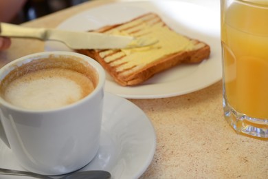 Photo of Cup of coffee and delicious sandwich with butter on beige table, closeup