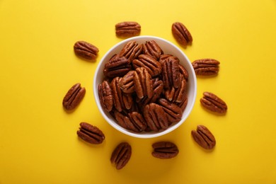 Bowl with tasty pecan nuts on yellow background, flat lay