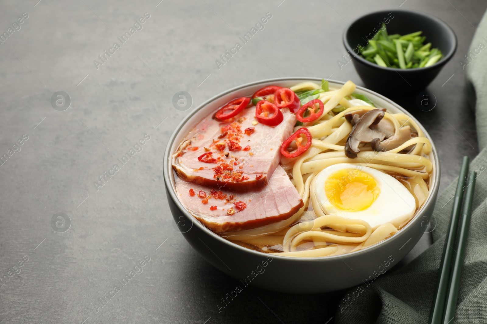 Photo of Delicious ramen in bowl and chopsticks on grey table, space for text. Noodle soup