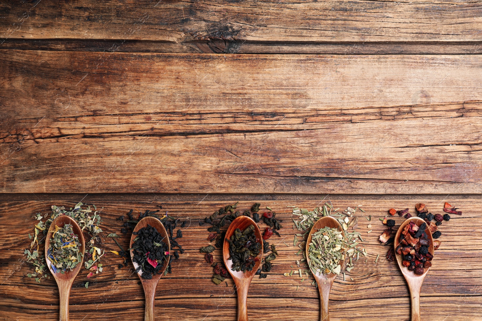 Photo of Flat lay composition with different teas and spoons on wooden table. Space for text