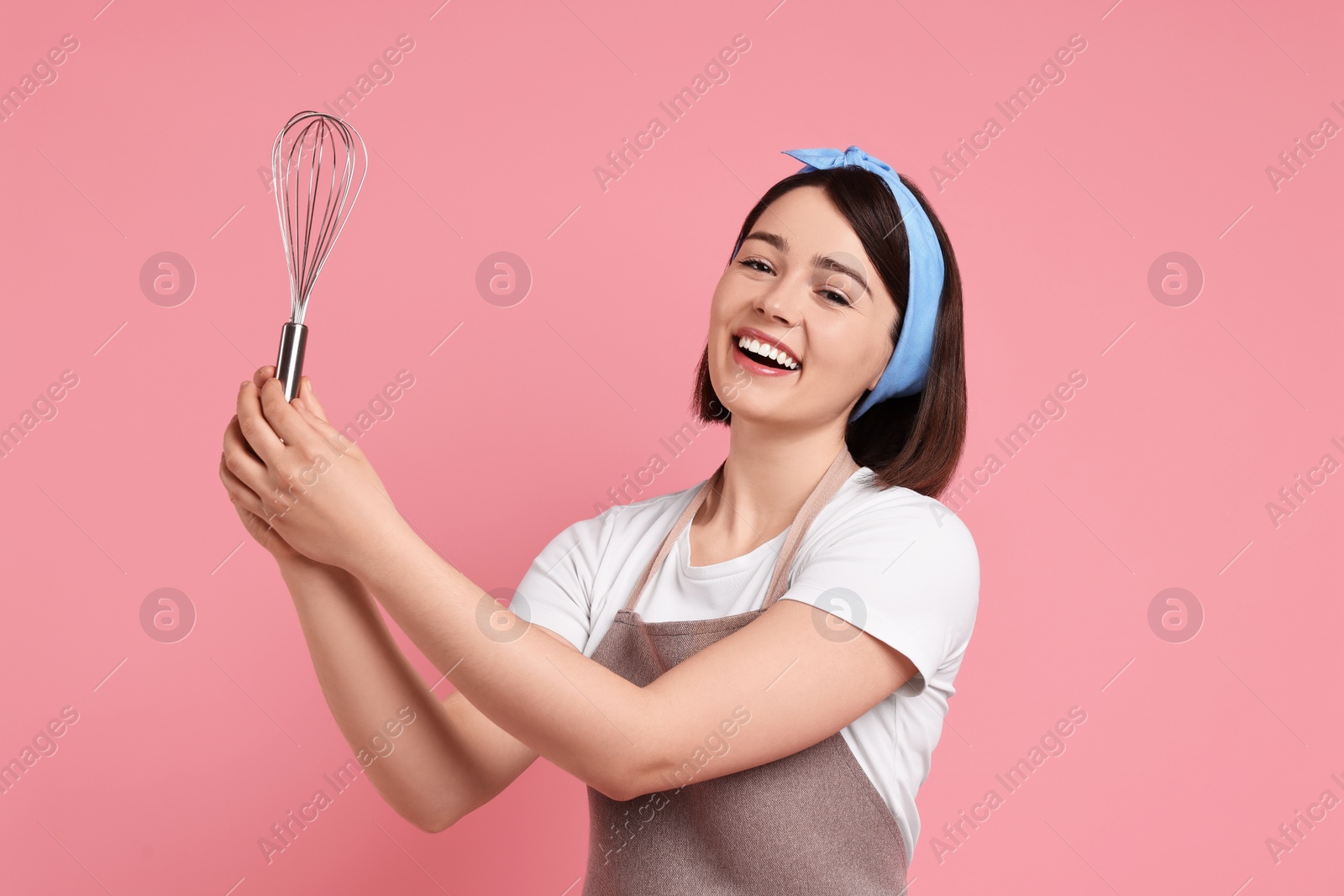 Photo of Happy confectioner with whisk on pink background