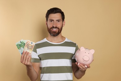 Photo of Happy man with money and ceramic piggy bank on beige background
