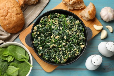 Photo of Tasty spinach dip with eggs in dish served on light blue wooden table, flat lay