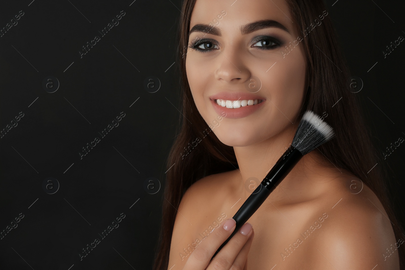 Photo of Portrait of beautiful woman with makeup brush on dark background. Space for text