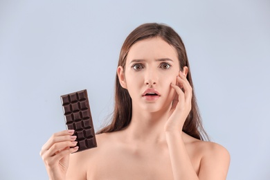 Photo of Teenage girl with acne problem holding chocolate bar against grey background