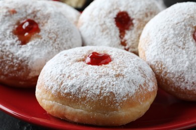 Photo of Delicious donuts with jelly and powdered sugar on red plate, closeup