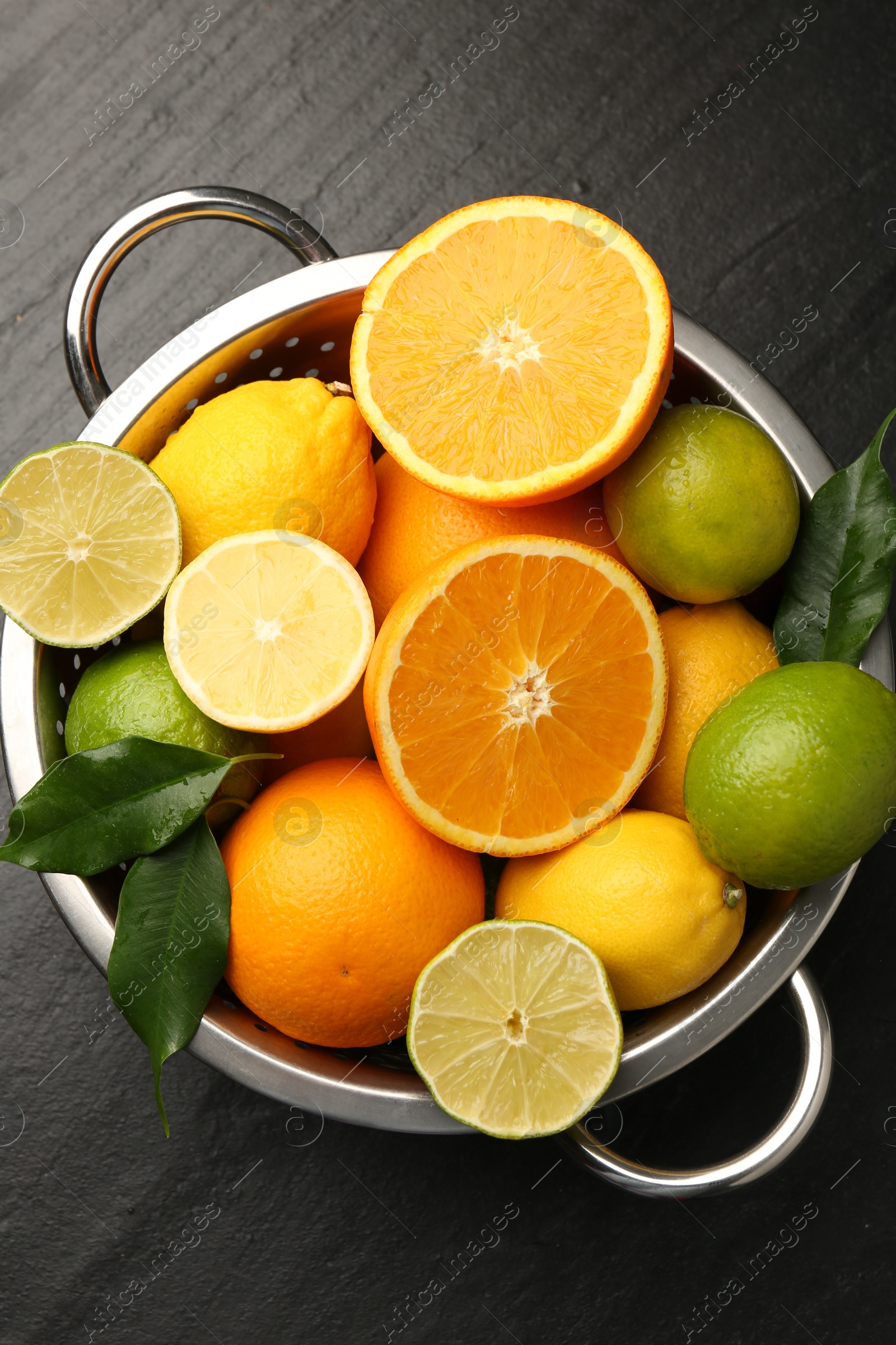 Photo of Fresh citrus fruits in colander on dark textured table, top view