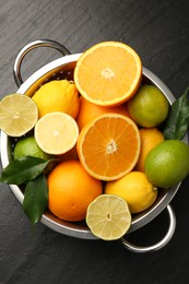 Photo of Fresh citrus fruits in colander on dark textured table, top view