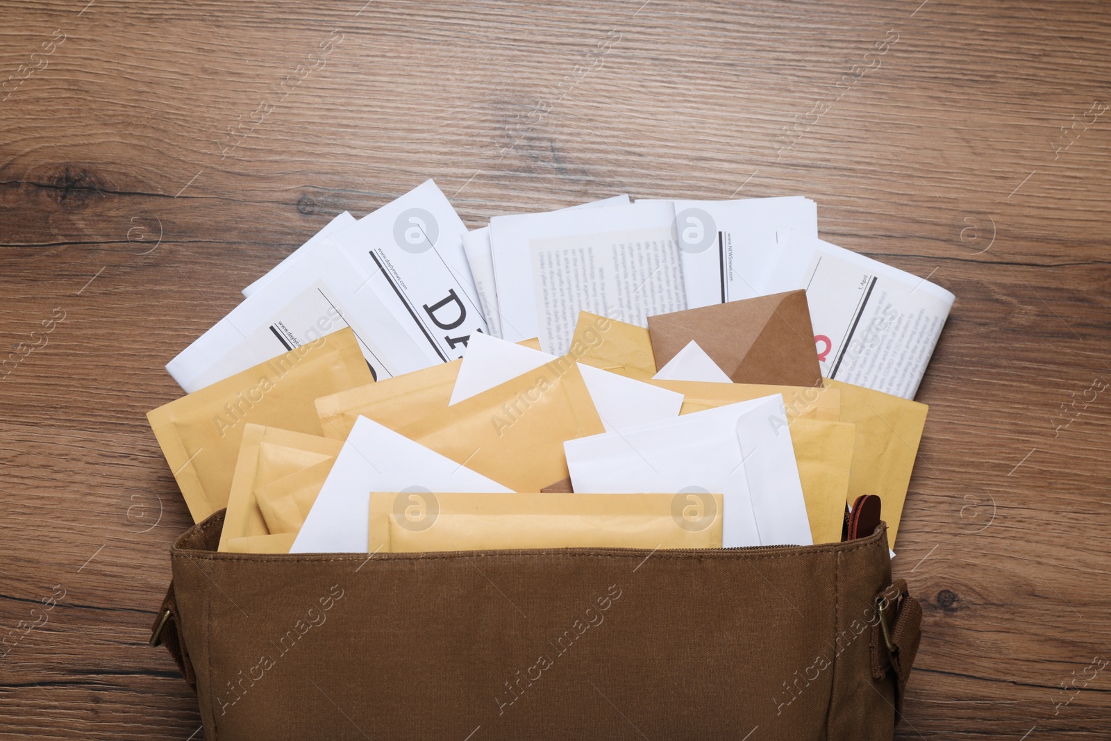 Photo of Brown postman bag with newspapers and mails on wooden table, flat lay