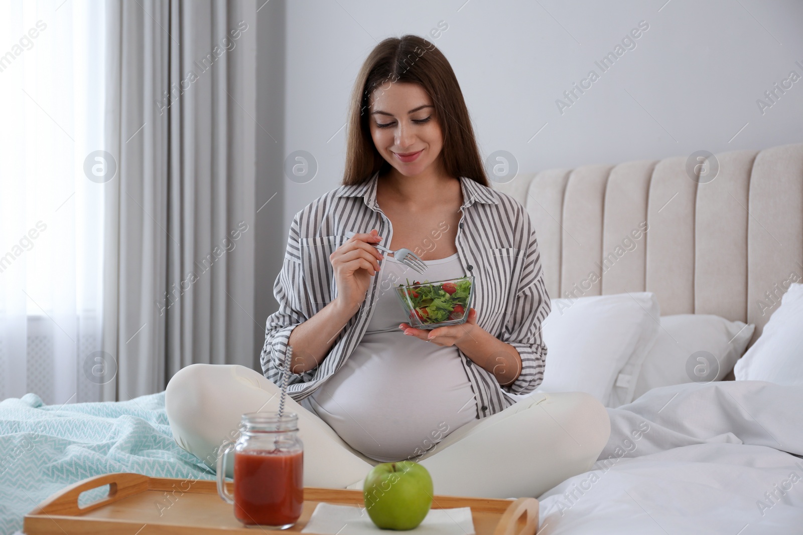 Photo of Pregnant woman eating breakfast on bed at home. Healthy diet