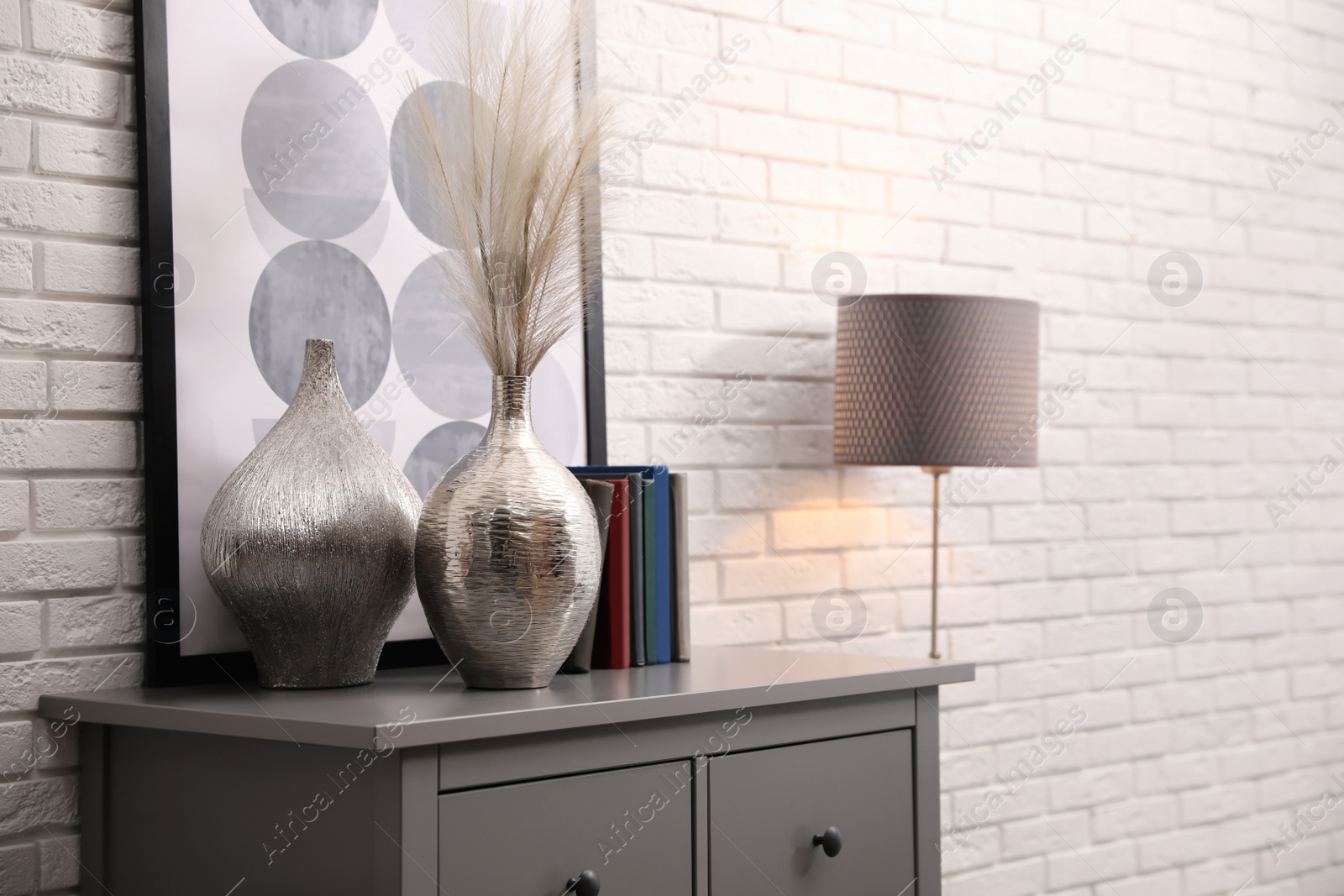 Photo of Grey chest of drawers with decor and books near white brick wall. Interior design