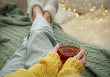 Photo of Woman with cup of tea sitting on plaid indoors, closeup