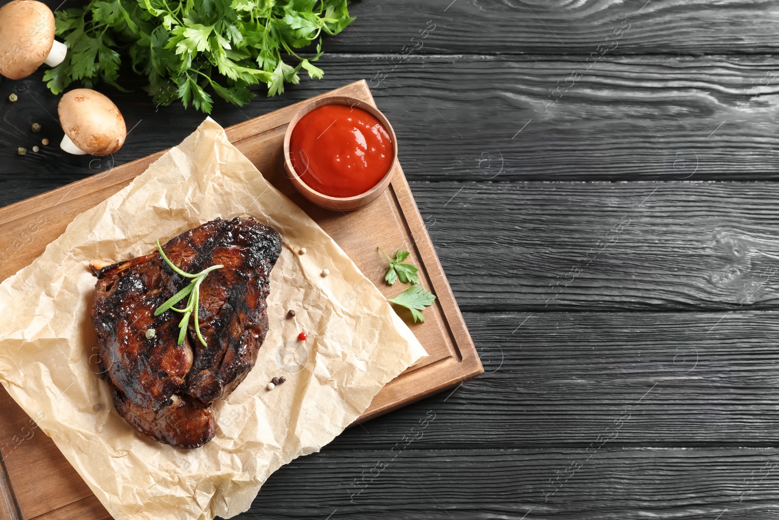 Photo of Board with barbecued steak and sauce on wooden background, top view. Space for text