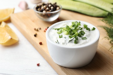 Photo of Ceramic bowl of cucumber sauce with ingredients on wooden table, space for text. Traditional Tzatziki