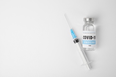 Vial with coronavirus vaccine and syringe on white background, flat lay. Space for text