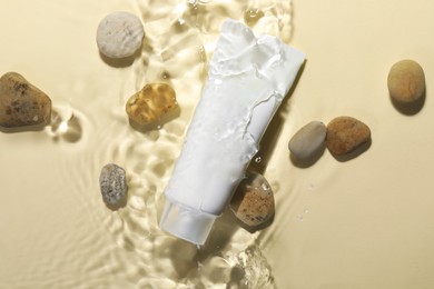 Photo of Tube of face cleansing product and stones in water against beige background, flat lay