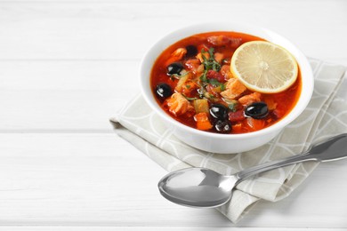 Photo of Meat solyanka soup with sausages, olives, vegetables and spoon on white wooden table, space for text