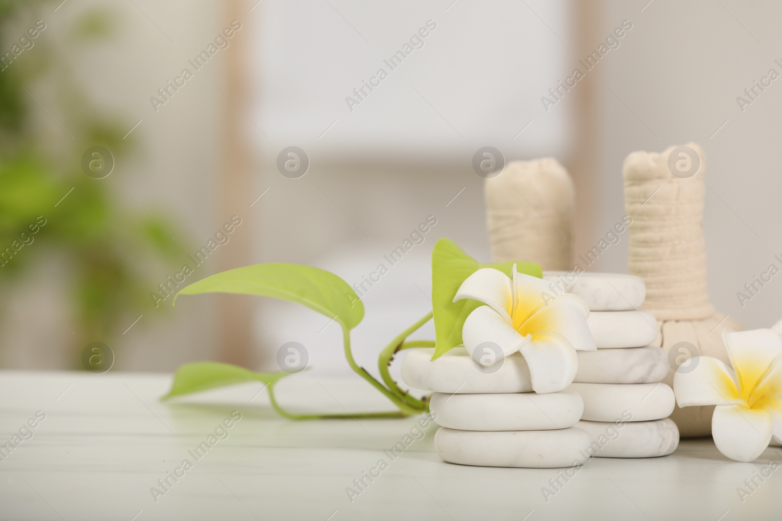 Photo of Spa composition. Herbal bags, stones, plumeria flowers and green leaves on white marble table, space for text