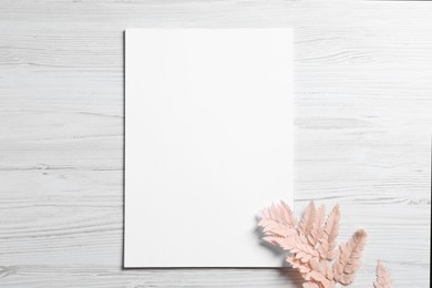 Photo of Empty sheet of paper and dry decorative leaves on white wooden table, flat lay. Mockup for design