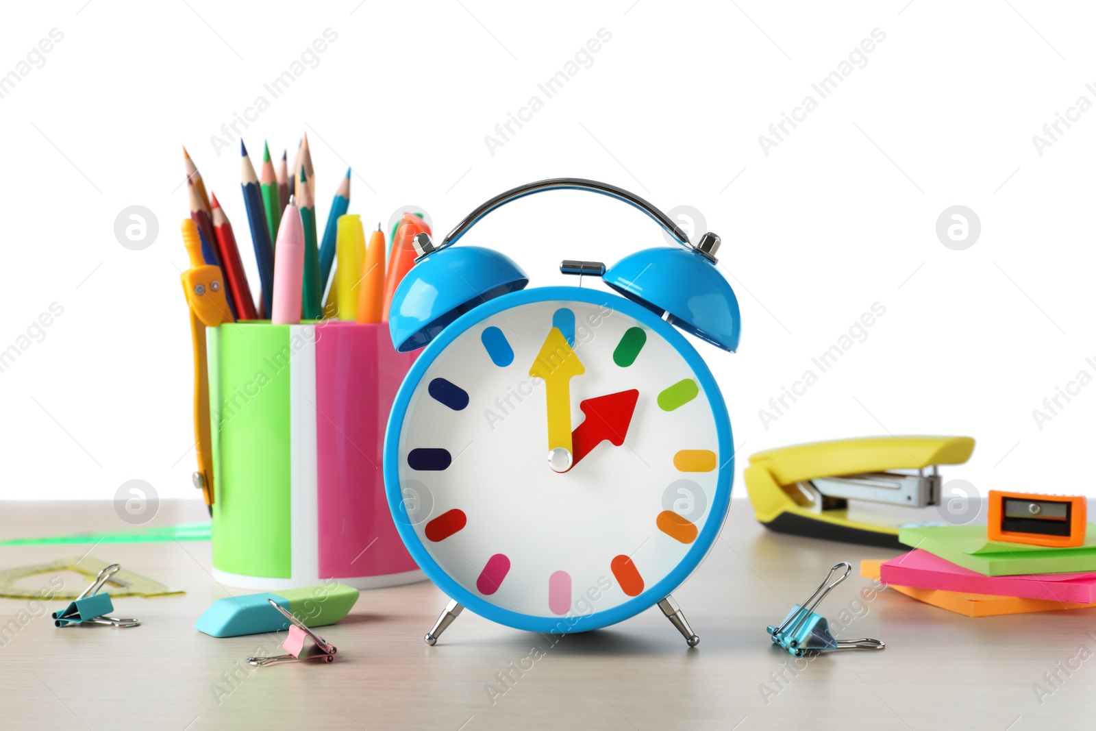 Photo of Light blue alarm clock and different stationery on wooden table against white background. School time