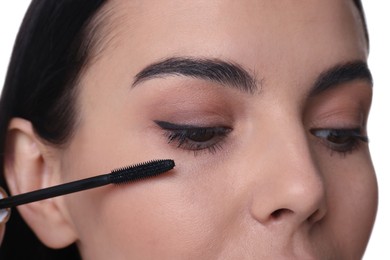 Photo of Beautiful young woman applying mascara on white background, closeup