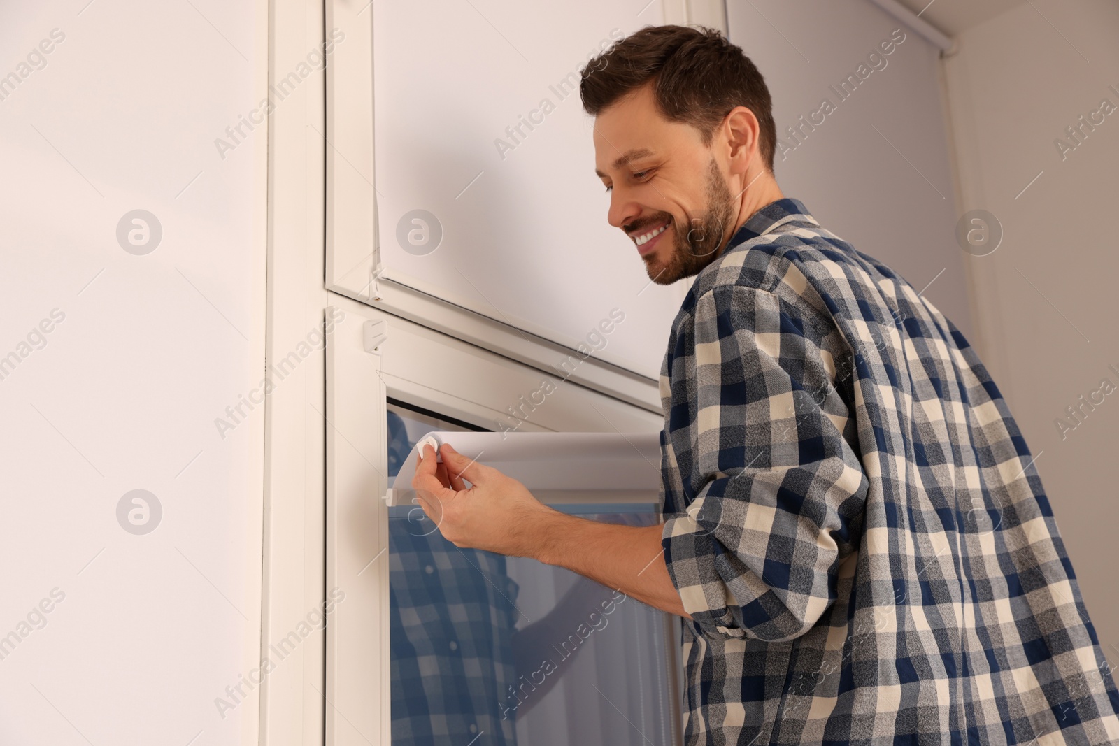 Photo of Man installing modern roller window blind indoors