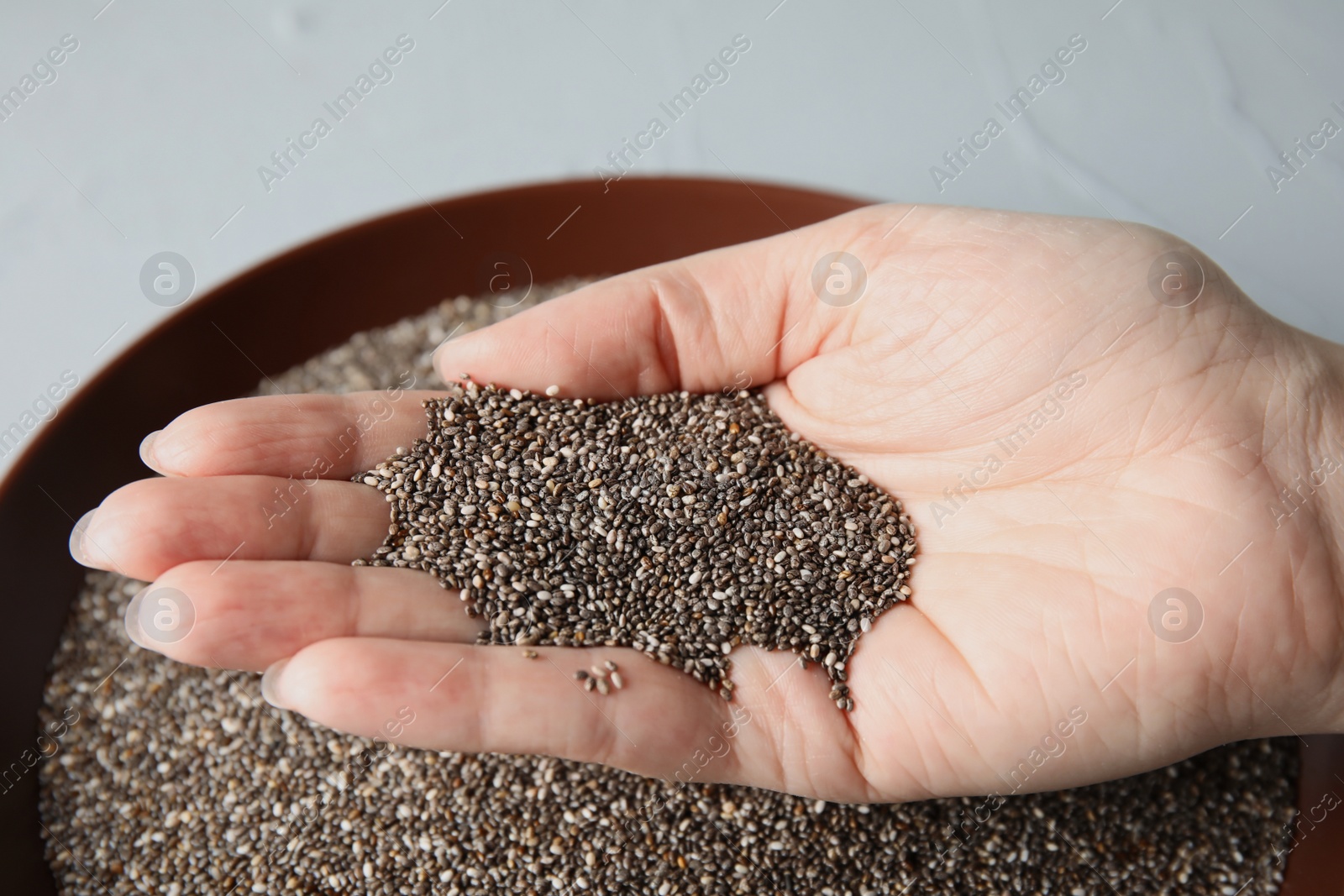 Photo of Woman holding heap of chia seeds over bowl on grey background, closeup